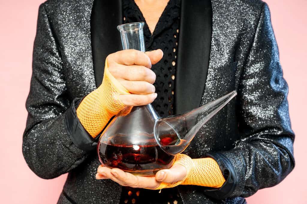 Person holding a decanter in stylish outfit.